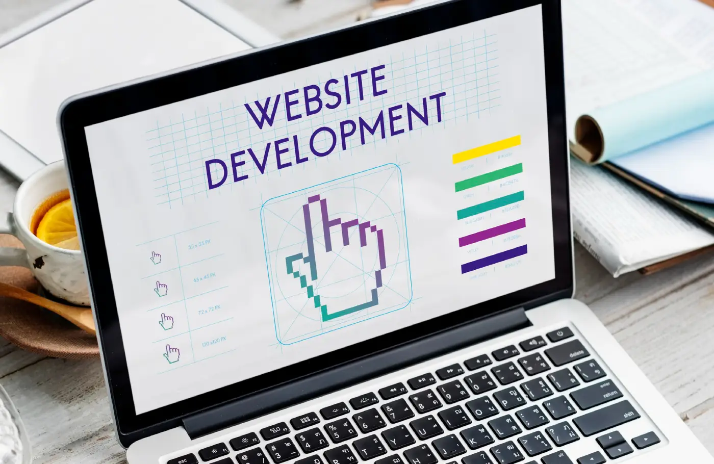 A laptop displaying a _Website Development_ design with a pixelated hand icon, surrounded by coffee and stationery on a wooden table A laptop displaying a _Website Development_ design with a pixelated hand icon, surrounded by coffee and stationery on a wooden table