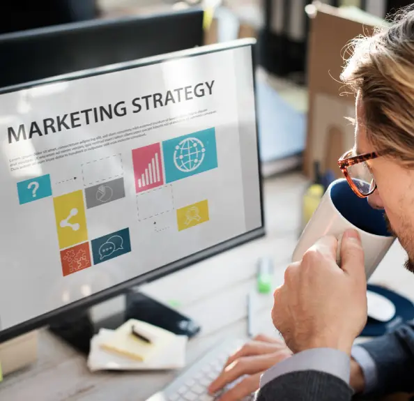 A person sits at a desk, sipping from a mug, while focused on a computer screen displaying a marketing strategy presentation A person sits at a desk, sipping from a mug, while focused on a computer screen displaying a marketing strategy presentation