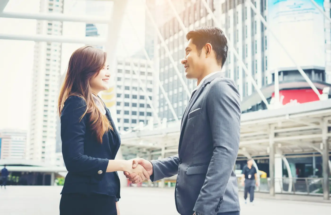 A woman in a suit shakes hands with a man in formal attire, set against a modern cityscape with skyscrapers in the background A woman in a suit shakes hands with a man in formal attire, set against a modern cityscape with skyscrapers in the background
